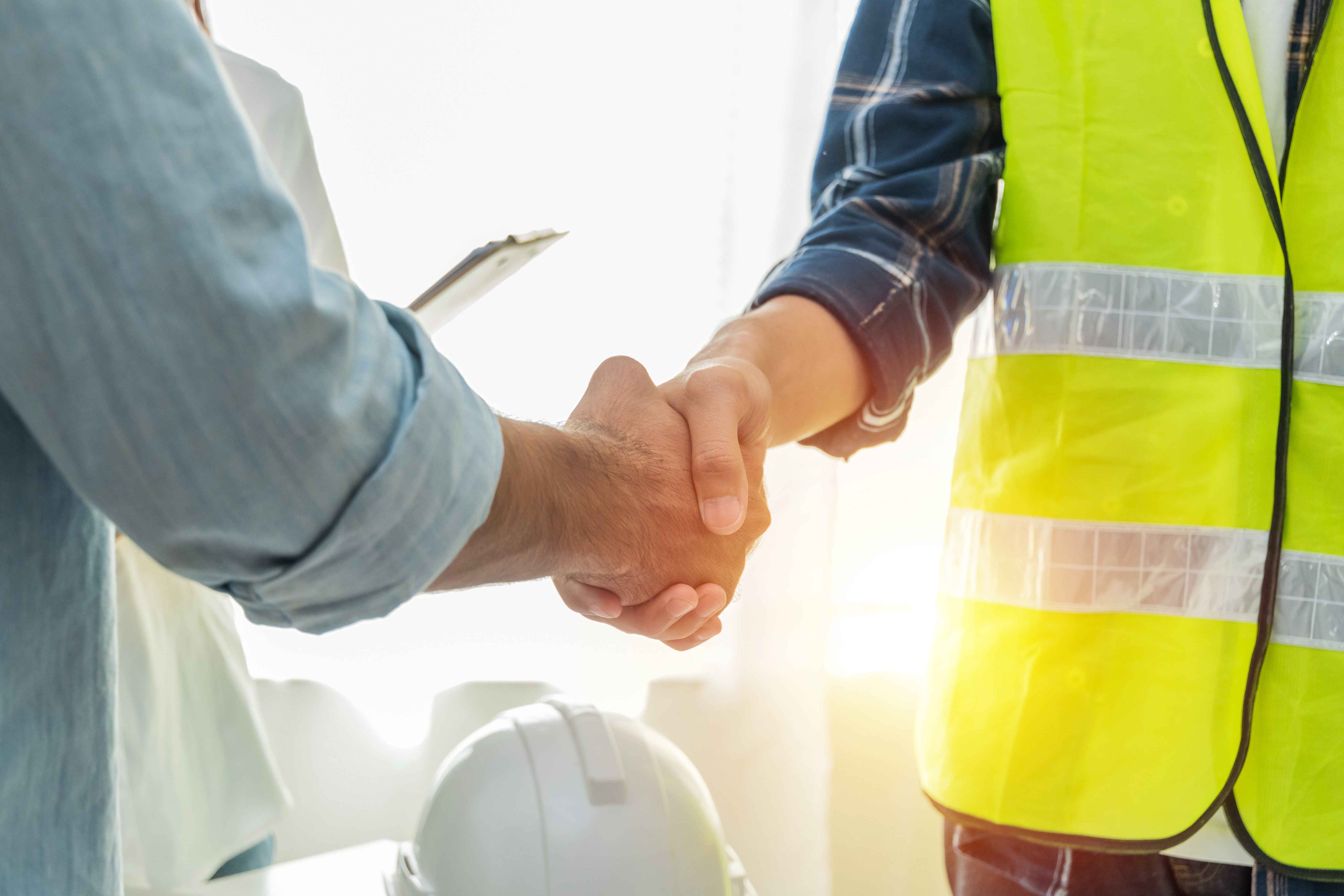 Contractor.-construction-worker-team-hands-shaking-after-plan-project-contract-on-workplace-desk-in-meeting-room-office-at-construction-site,-contractor,-engineering,-partnership,-construction-concept-1321891103